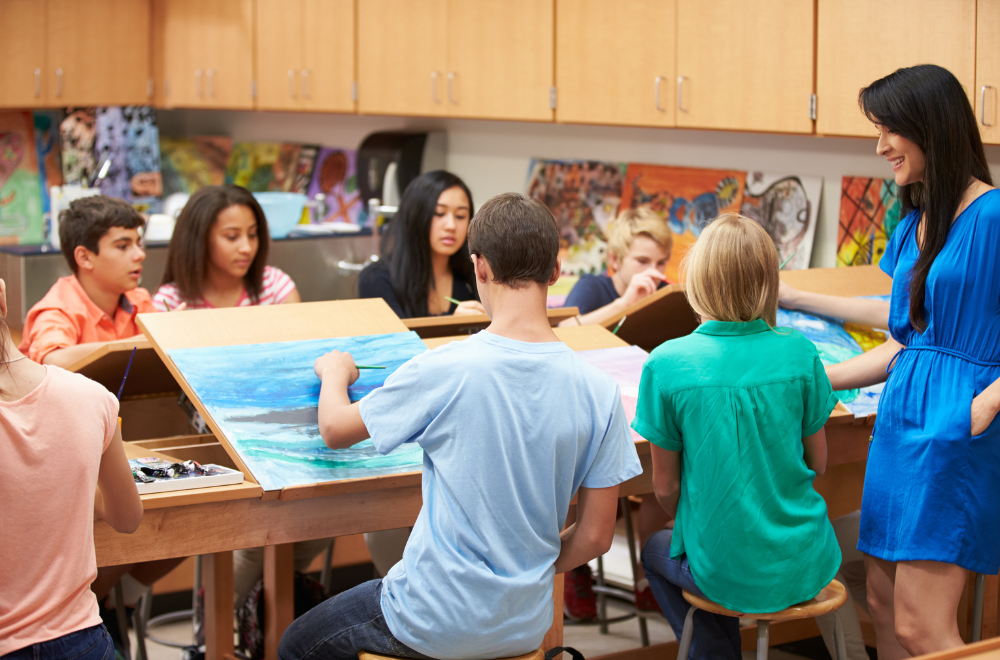 kids painting at easels with a woman in a blue dress standing by