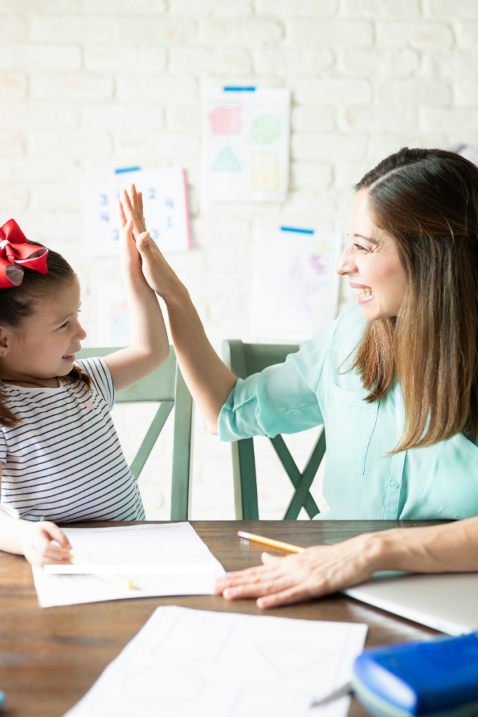 Mom and young daughter high-fiving at a table with a worksheet and pencils